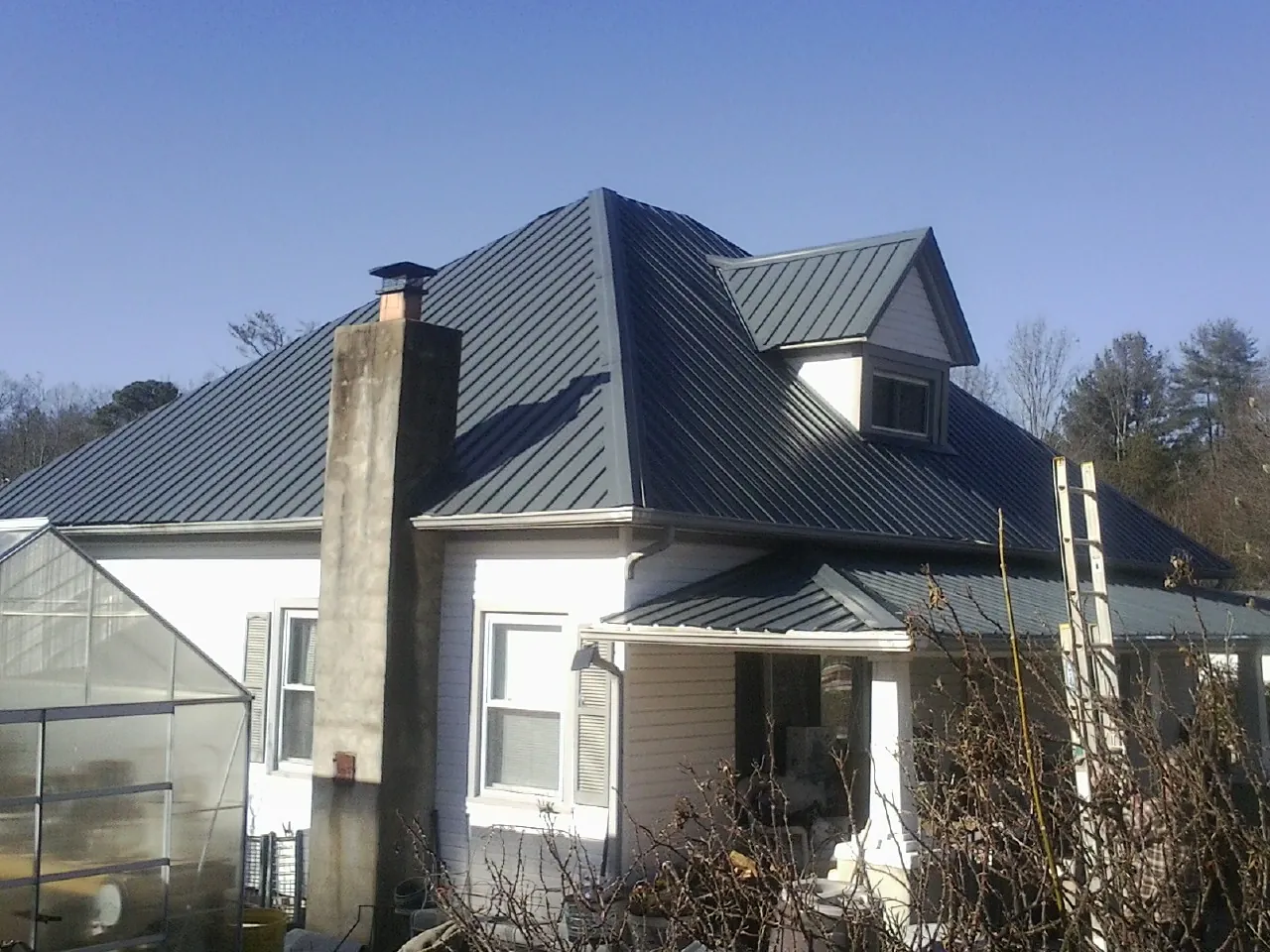 Dark blue standing seam metal roof on a white farmhouse with dormer — Slate & Tile Roof Repair by Roofing Brothers in Helmville