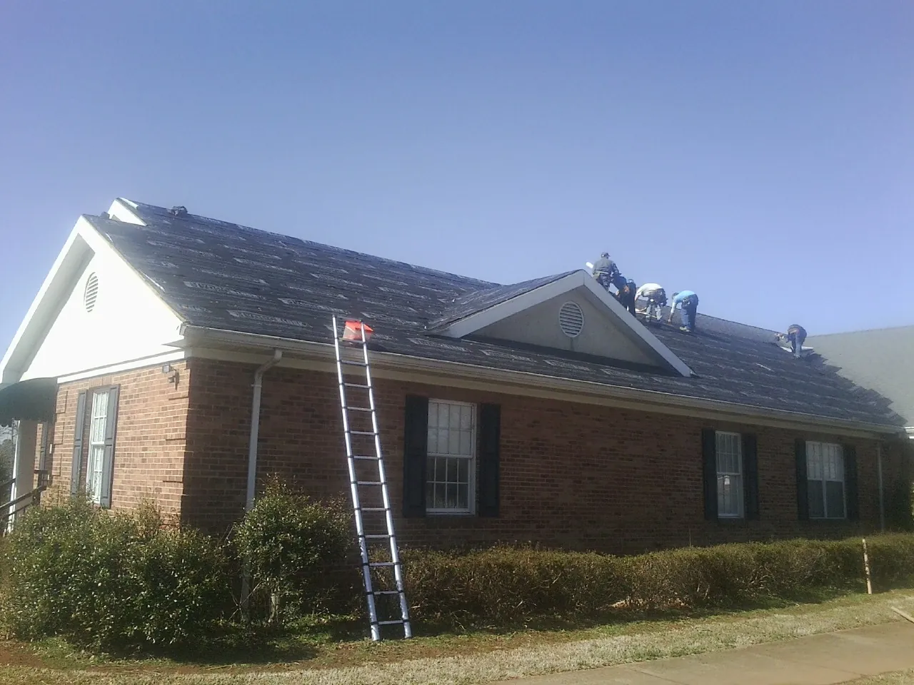 Crew tearing shingles off a brick ranch roof with a ladder set — Emergency Roof Repair work by our crew in Helmville