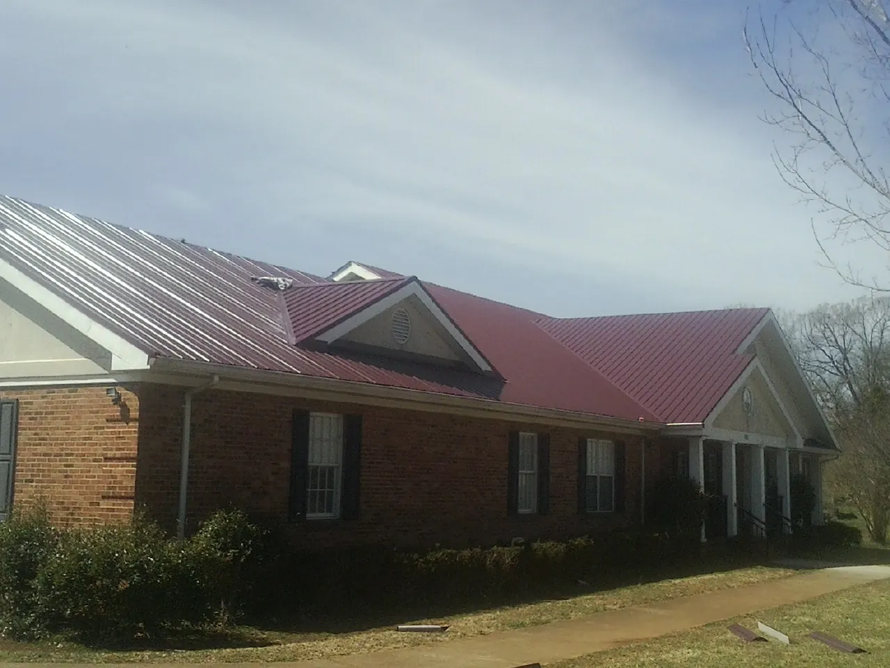 Red metal roof with gabled entries on a long brick building, from a Hail Damage Roof Repair job in Helmville