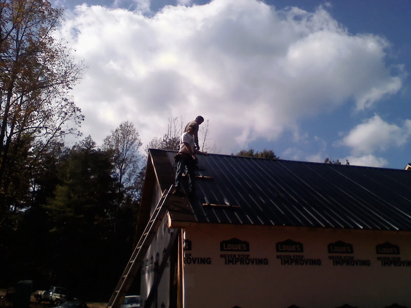 Roofer fastening dark metal panels high against a cloudy sky, from a Roof Inspection job in Helmville